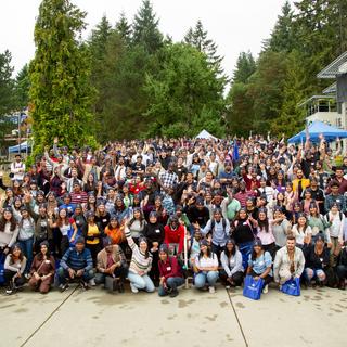 About 200 students sit on a set of stairs outside at a university campus. 