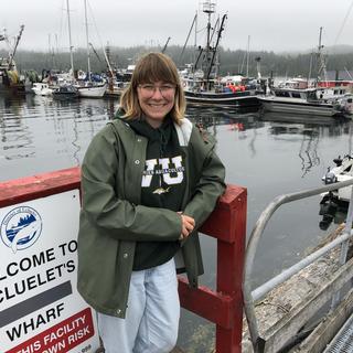 Allie Unger leans against a railing at Ucluelet harbour with boats anchored in the background.