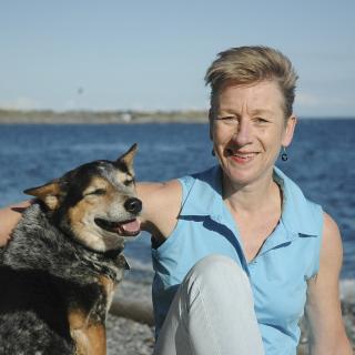 Debra Hellbach sits on the beach with a dog.