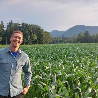 Douglas Groenendijk grins while standing in a vast green field with a mountain range behind him.