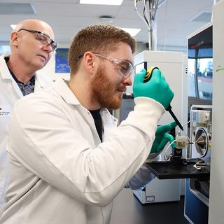 Dr. Chris Gill observes as Lucas Abruzzi puts a sample in the mass spectrometer.