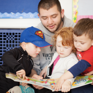 An early childhood educator reading a book to three kids