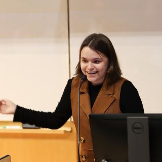 A student holds their right arm out and smiles.