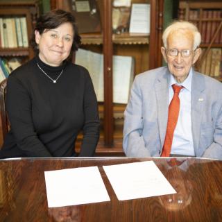 Deborah Saucier and Stephen Jarislowsky signing documents seated at a table