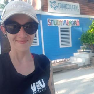 Melanie stands in front of the Tobacco Caye sign, which reads Study Abroad underneath it