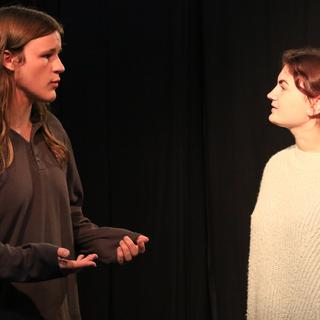 Two actors face each other on stage while rehearsing a scene.