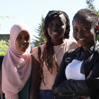 Facing the camera and standing from left to right are refugee students Hanan Ali Abdi, Nyagua Deng Goch, and Daniella (Sifa) Mukenge