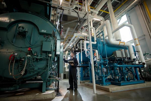 a power engineer inspects large tanks in a big machine room with sunlight peeking through the window