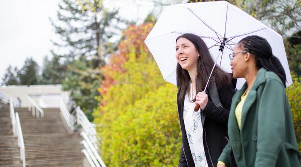 Two students walk near the stairs at VIU, one carries an umbrella