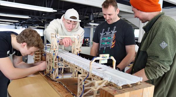 Four students bend over a bridge structure together