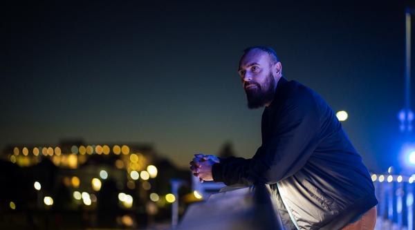 Shanon Sinn leans on a balcony railing and gazes at a night city scape