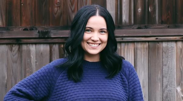 Alisha wearing a blue sweater standing in front of a fence