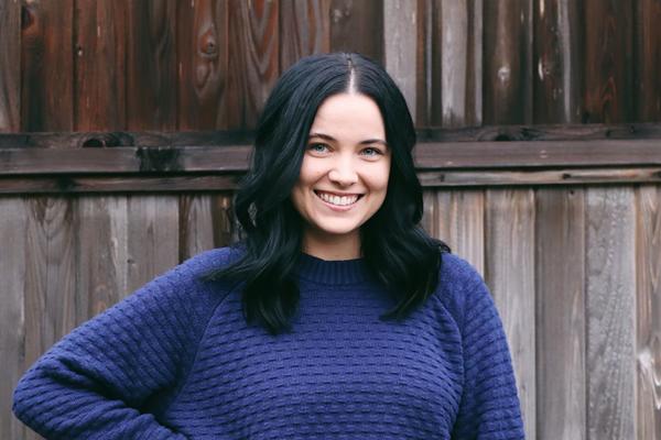 Alisha wearing a blue sweater standing in front of a fence