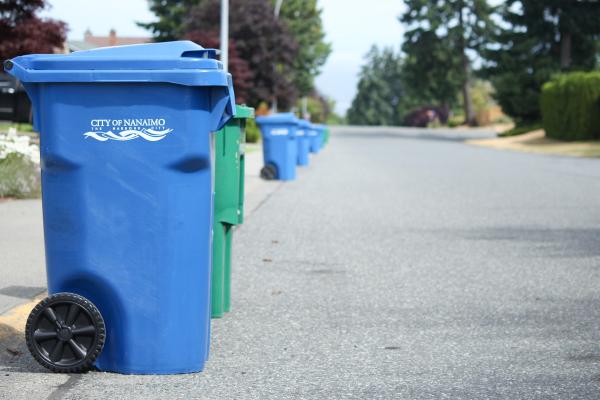 Blue garbage bins and green recycling bins line the left side of a Nanaimo street.