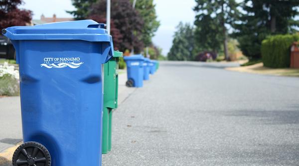 Blue garbage bins and green recycling bins line the left side of a Nanaimo street.