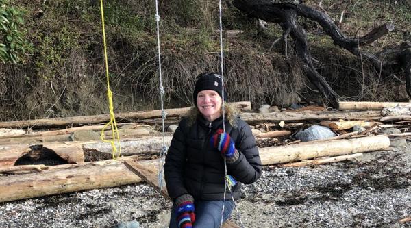 Christin Collishaw sitting outside in a swing at beach and smiling at the camera