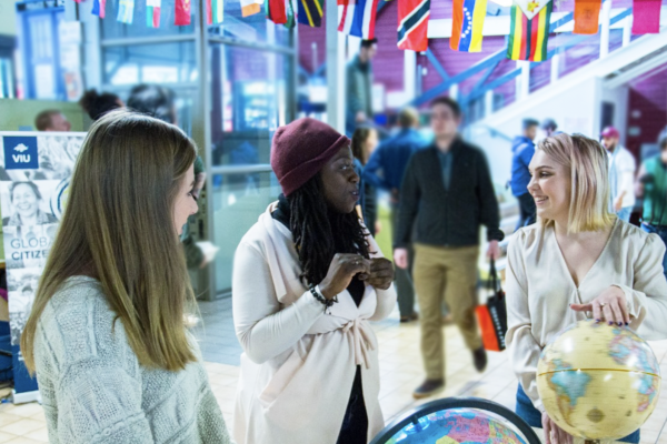 Three woman standing and chatting in front of a table on which sits two globes.