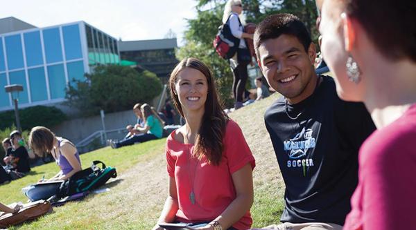 Three students sitting on lawn interacting with each other