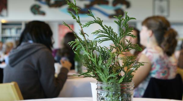 Cedar branch in a jar in foreground, people in VIU's Gathering Place in background