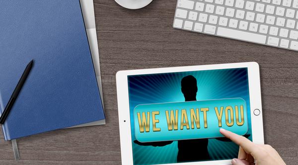 keyboard, ipad that says We Want You, folders, pens and cup of coffee on a desk