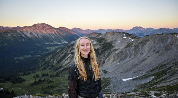 Kelsey Moore smiles with a mountain range at sunset behind her.