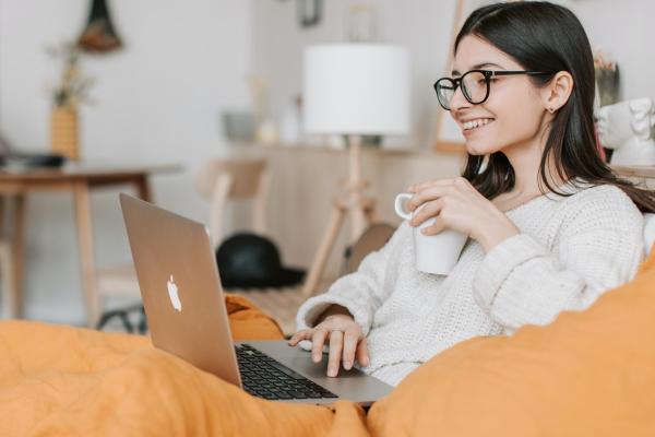 Woman smiles at her laptop screen, holding a cup of coffee