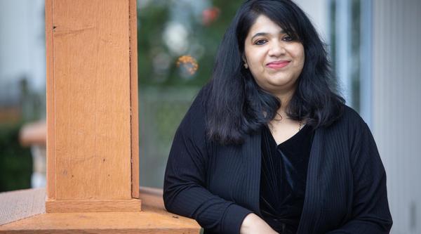 A woman leans on a pillar and smiles into the camera