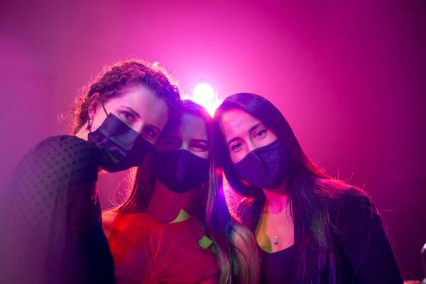 Three women posing in masks with a stage light behind them