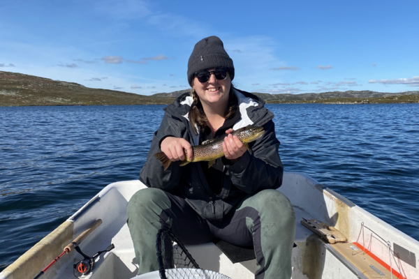 Sarah Osborne sitting in a boat holding a fish and smiling at the camera