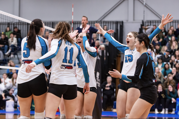 A group of VIU Mariners women's volleyball teammates celebrate in a circle on the volleyball court