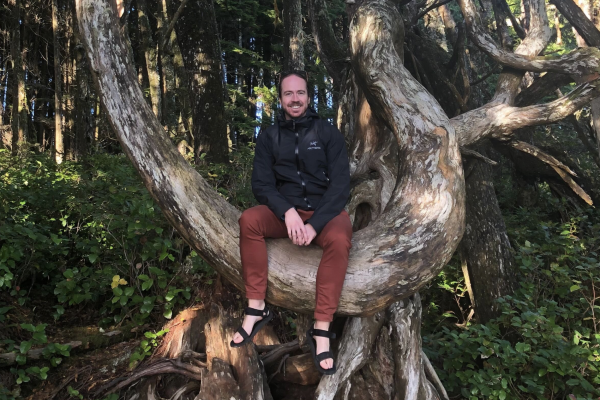 Dr. Michael Asmussen sitting in a tree and smiling at the camera.