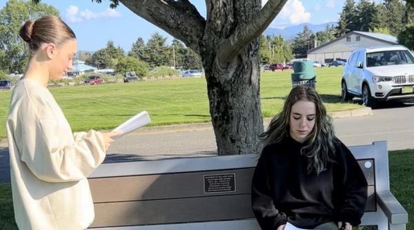 Two actors rehearse with scripts in their hand near a bench in a park.