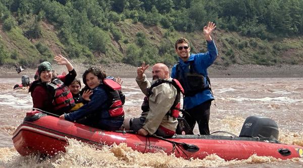 Lucas Gamp in a raft on a river with clients waving at the camera