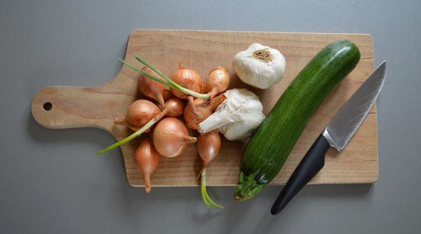 A cutting board with onions, garlic and zucchini