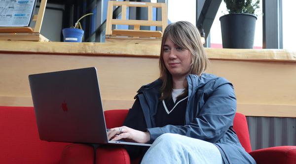 Young woman sitting on a red couch looking at a laptop