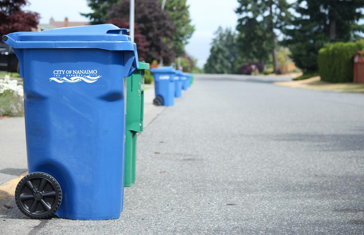 Blue garbage bins and green recycling bins line the left side of a Nanaimo street.