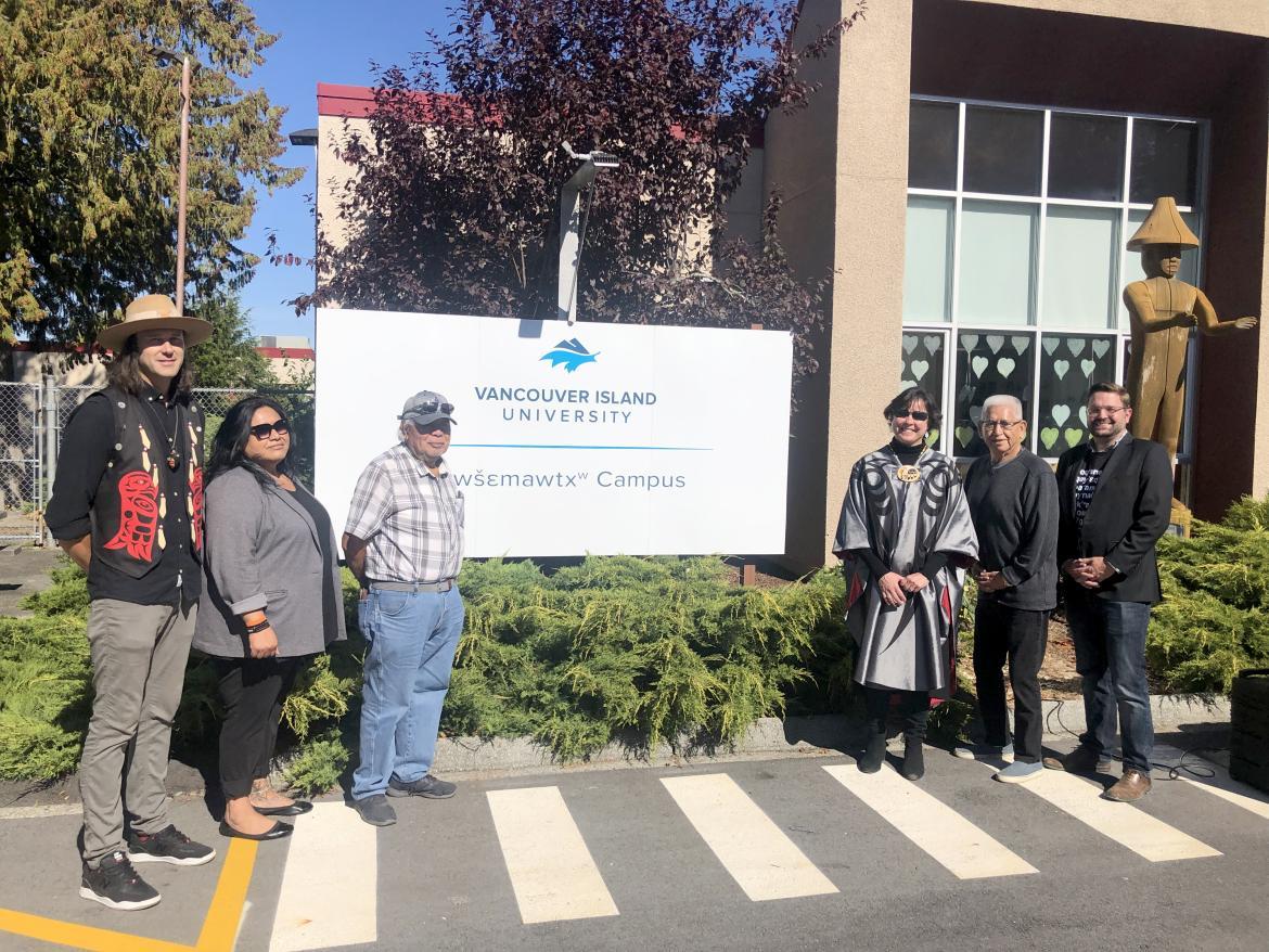 People standing in front of a sign announcing the renaming of a campus.