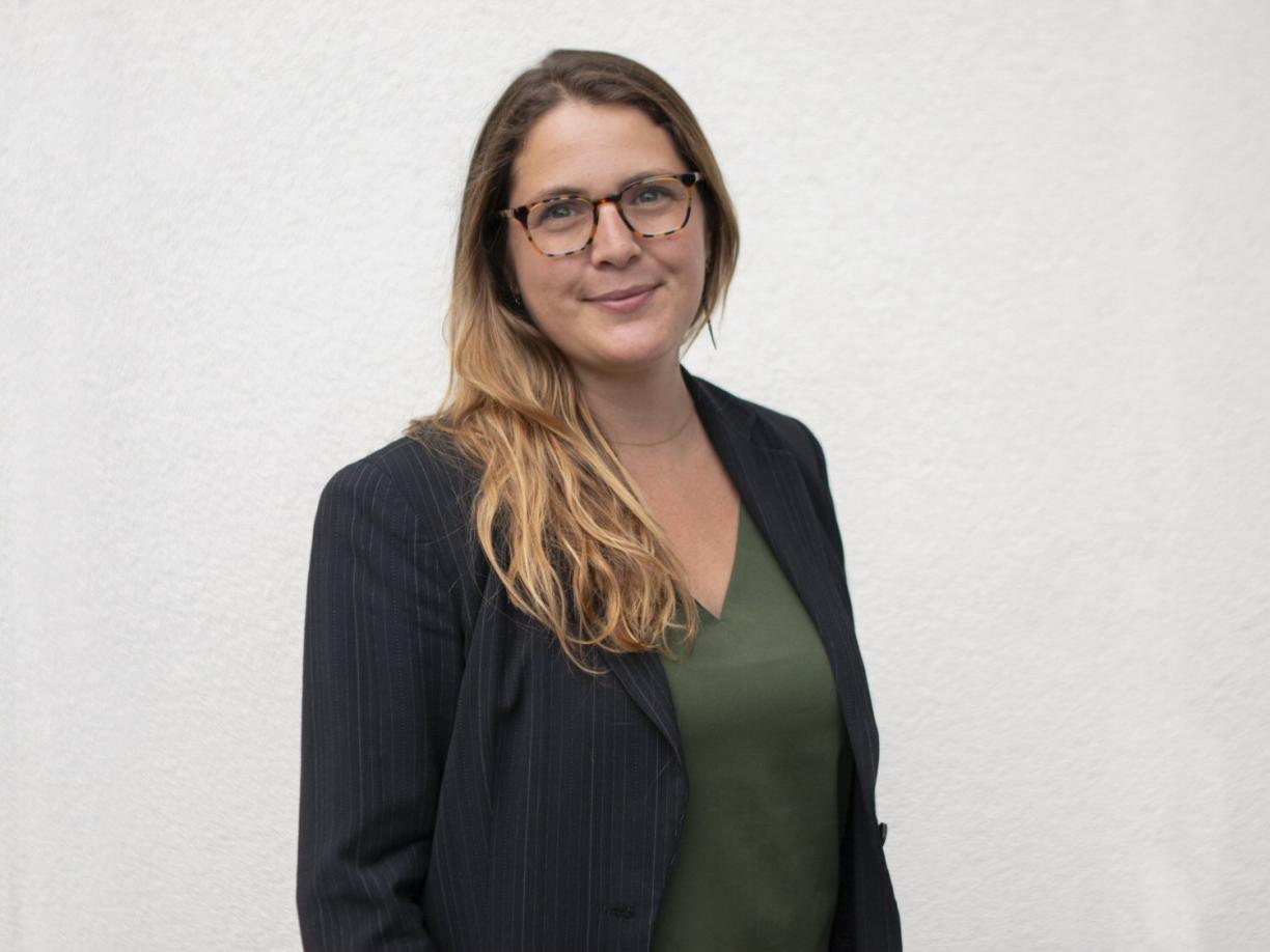 Dr. Amanda Wager, wearing a green shirt and black blazer, stands in front of a white wall.