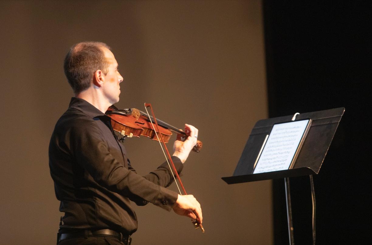 James Mark plays a violin while looking at a stand with sheet music on it.