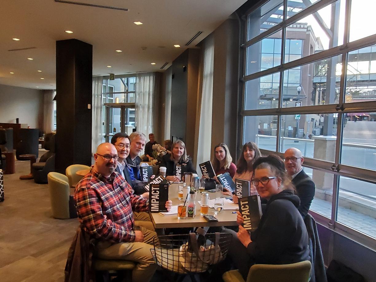 A group of people sit at a table, all holding copies of the same book