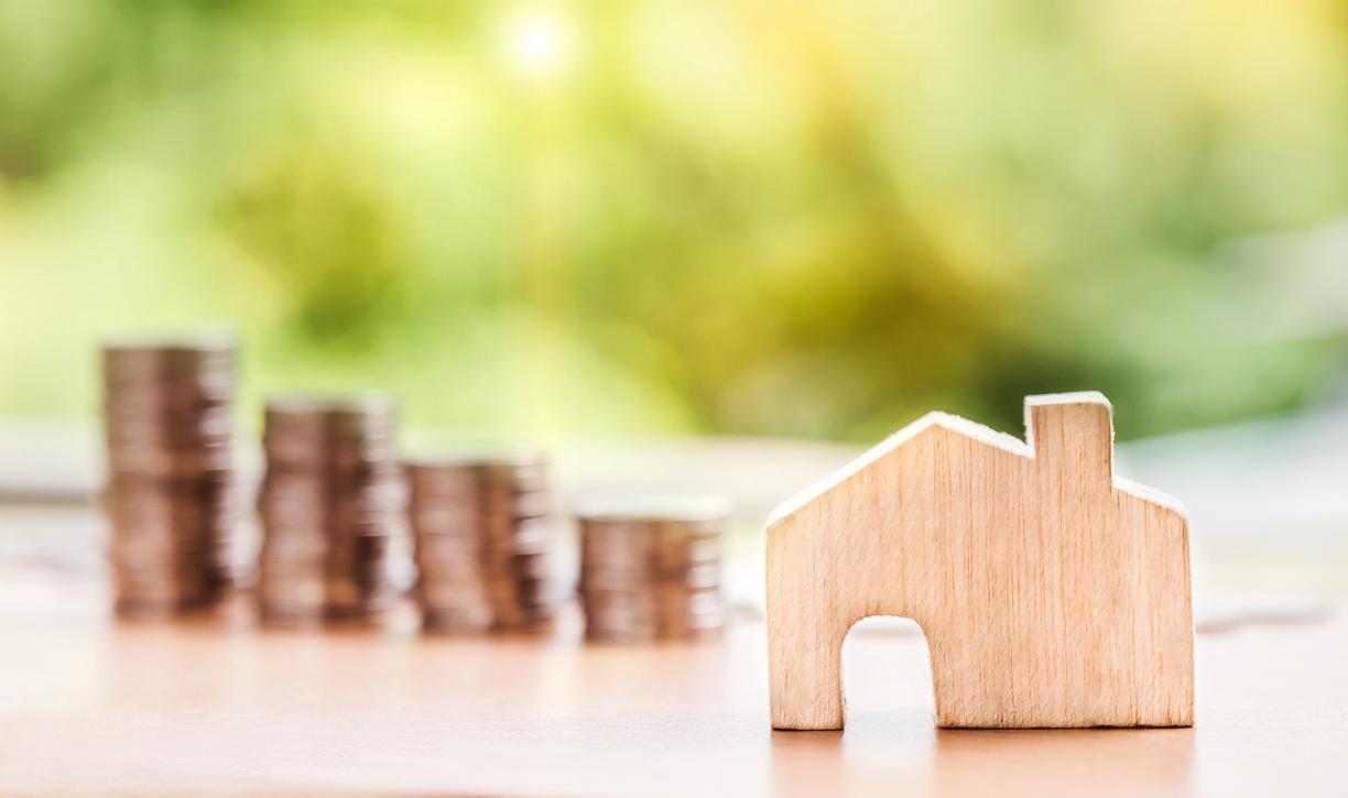 A wooden cutout of a house with four stacks of coins behind it.