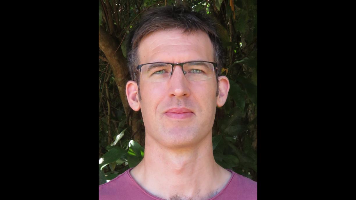 Sean Sloan faces the camera while standing in front of a canopy of trees.