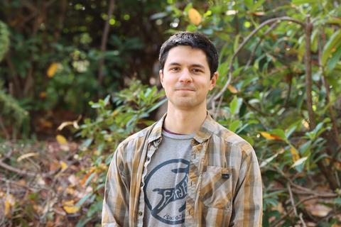 Joe Clark stand in front of a lush green bush at the VIU Nanaimo campus.