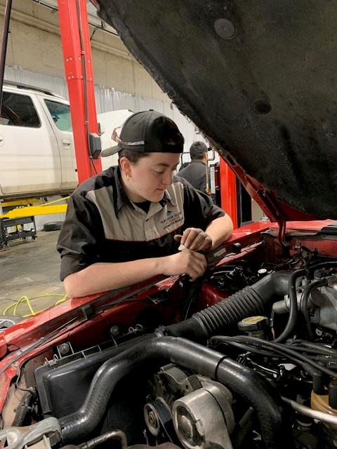 Trinity looks at the engine of a car